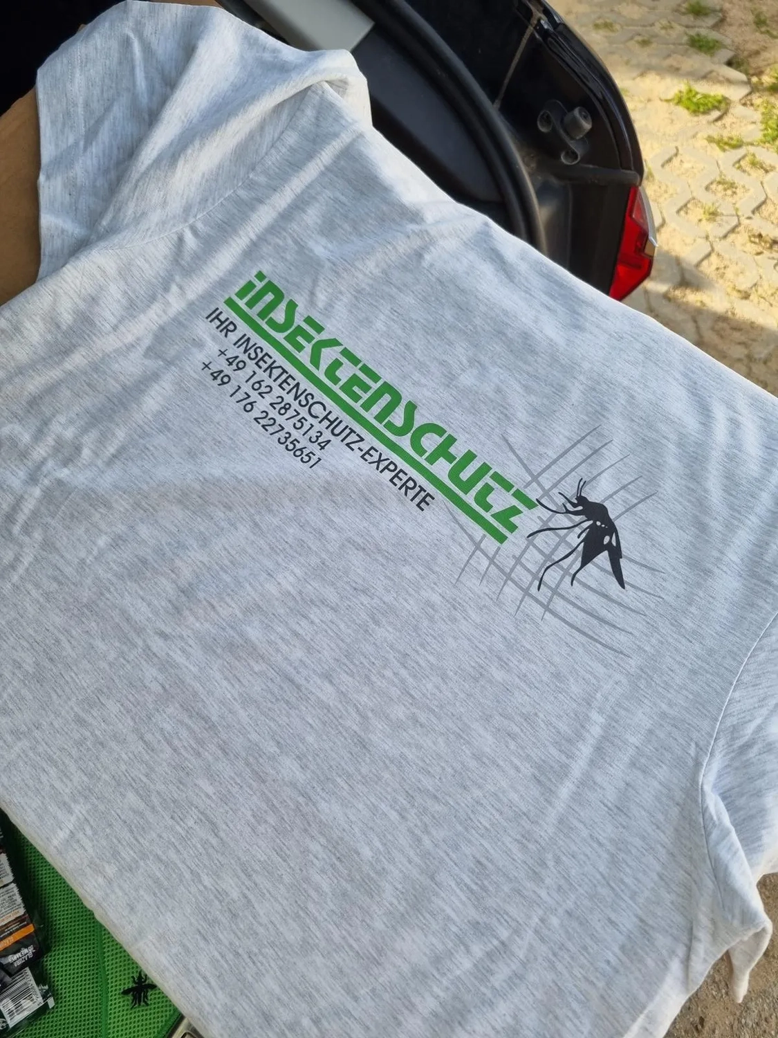 Cybulski Trockenbau - Bau und Fensterbauer - Ein hellgraues T-Shirt mit einem grün-schwarzen Logo auf dem Rücken, auf dem „INSEKTENSCHUTZ“ steht und das deutsche Telefonnummern enthält.