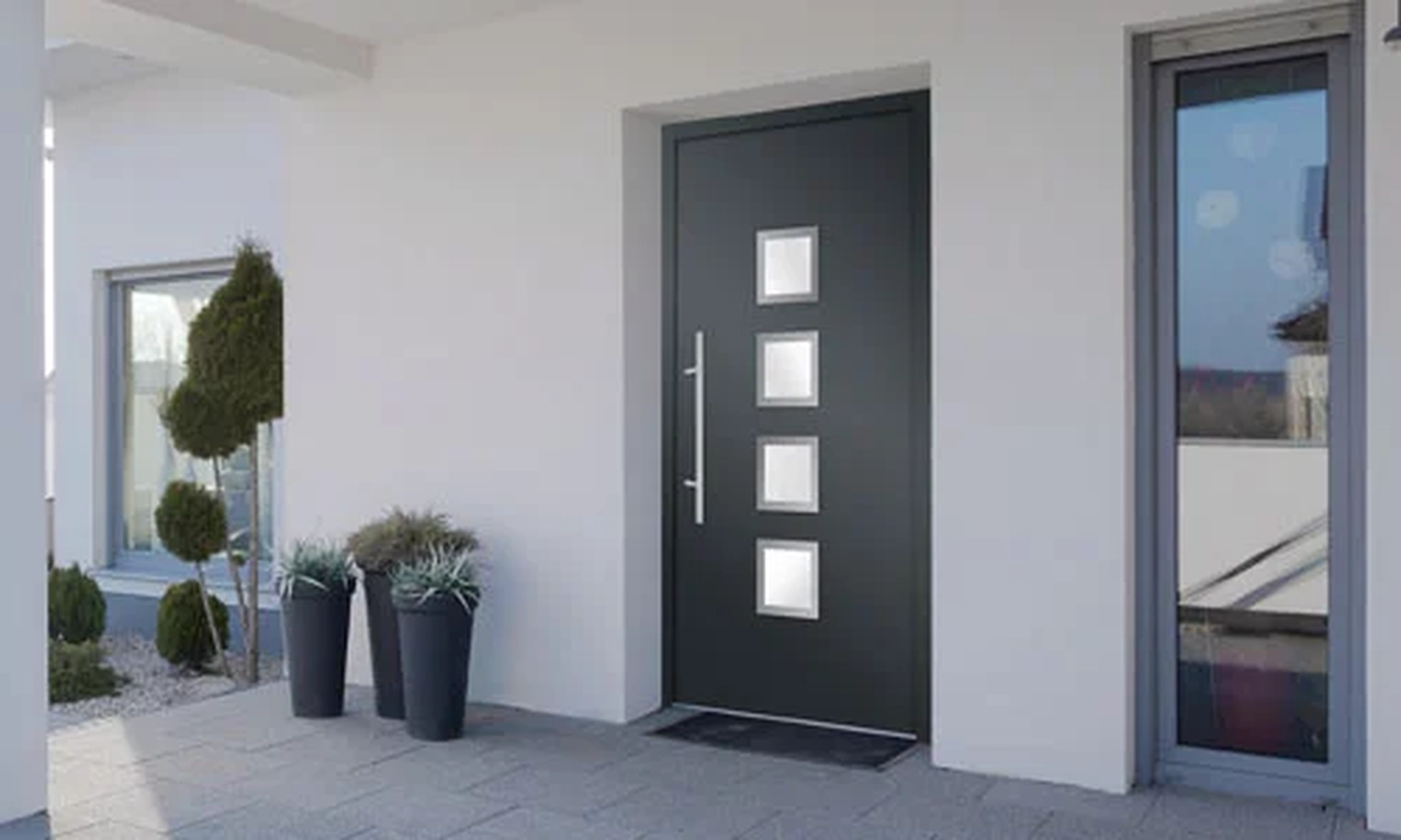 Cybulski Trockenbau - Bau und Fensterbauer - Moderne schwarze Haustür mit vier kleinen quadratischen Fenstern und einem langen silbernen Türgriff. Sicherheit und Design vereint.